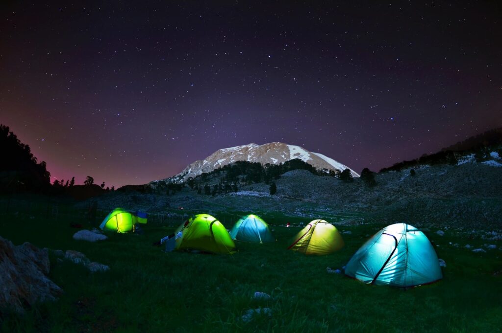 Several tents in a Vally lit internally by flashlights so they appear to be glowing in the foreground of a mountain. Reliable flashlights are important to have in your camping Safety and Emergency Gear.