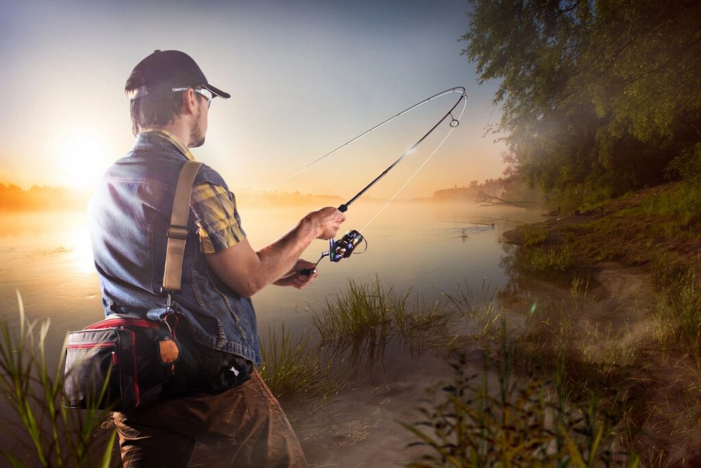 There is a man using a spinning fishing rod on a cool fall lake. The mist of the morning is rising across the water.